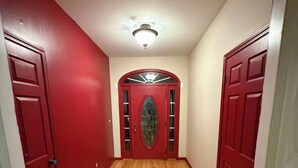 Un corridoio con pavimento in legno, porte rosse e un lampadario.