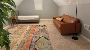 Una stanza con un letto, un divano in pelle marrone, un tappeto decorato, una lampada da terra e una ventola a soffitto.