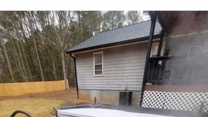 Un jacuzzi con asiento integrado y panel de control, rodeado por una terraza de madera y una cerca blanca.