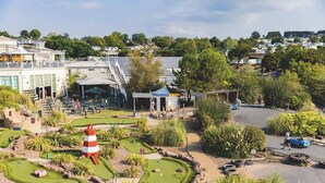 A golf course with a lighthouse, a building with outdoor seating, and a parking area. - The Pilots Rest Sleeps 6 (Exmouth)