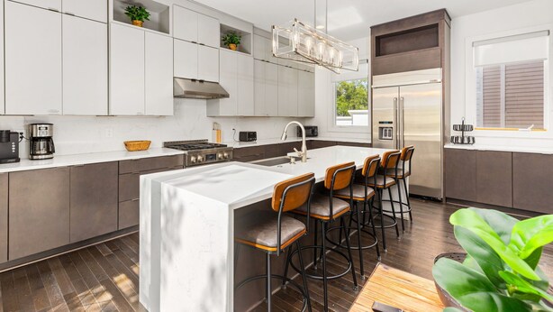Una cocina moderna con armarios blancos, un refrigerador de acero inoxidable y una barra con taburetes.