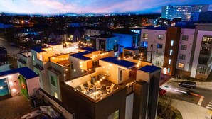 Un edificio de varios pisos con terraza en la azotea, equipada con asientos al aire libre y luces colgantes.