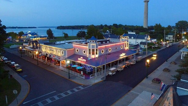 A waterfront building with a prominent tower, a docked boat, and a restaurant with outdoor seating. - Space to Laugh, Lounge & Live | 12 ppl | IC108 (Put-in-Bay)