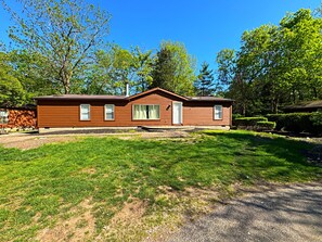 A single-story wooden house with a front porch, a small driveway, and a well-maintained lawn. - All New, All Comfort—Fits 12 ppl | IC110 (Put-in-Bay)