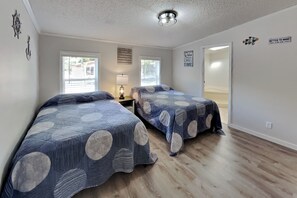 A bedroom with two beds, a nightstand, a lamp, and a window. - All New, All Comfort—Fits 12 ppl | IC110 (Put-in-Bay)