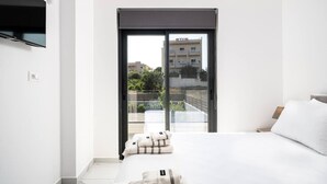 Ein modernes Hotelzimmer mit einem großen Bett, einem flachbildfernseher an der Wand und einer Glasschiebetür, die auf einen Balkon mit Blick auf die Stadt führt.