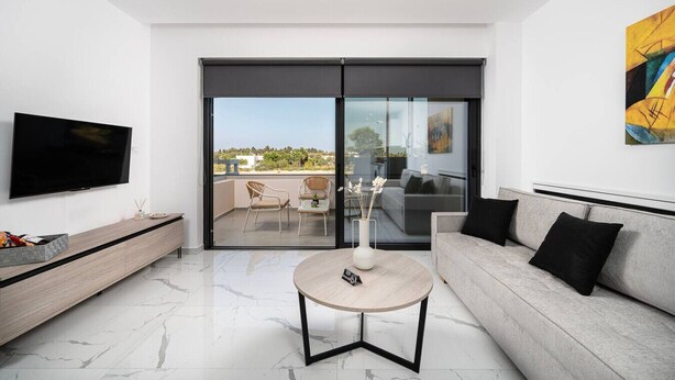 Ein modernes Wohnzimmer mit Flachbildfernseher, einer Couch, einem Couchtisch und einem Balkon mit Gartenmöbeln.