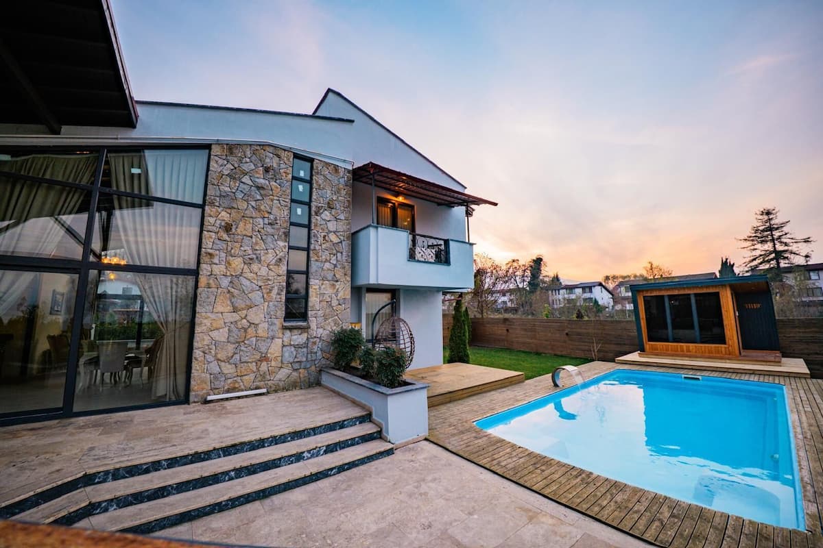 Una casa moderna con fachada de piedra, un balcón y una piscina.
