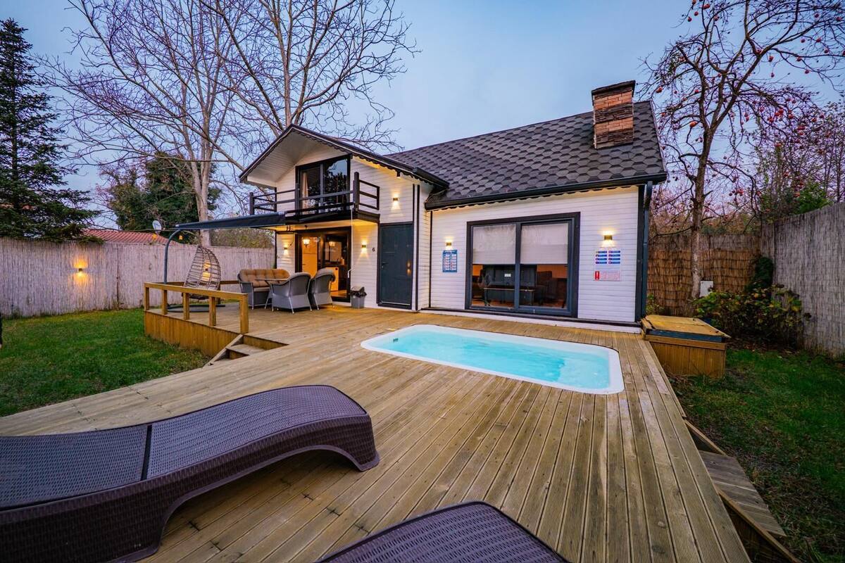 Una casa moderna con terraza de madera, bañera de hidromasaje y zona de estar al aire libre cubierta.