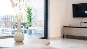Uma sala de estar moderna com um vaso branco sobre uma mesa de madeira, uma TV na parede e uma varanda com mobiliário de exterior.