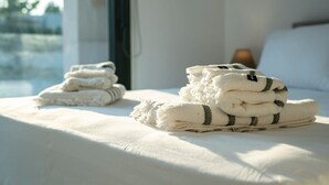 Cama bem arrumada com toalhas dobradas e vista para o exterior pela janela.