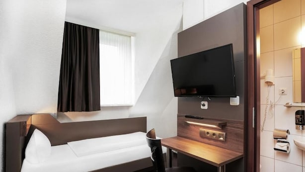 Une chambre d’hôtel moderne équipée d’un canapé-lit, d’un bureau avec un téléviseur à écran plat, d’une petite table et d’un miroir.