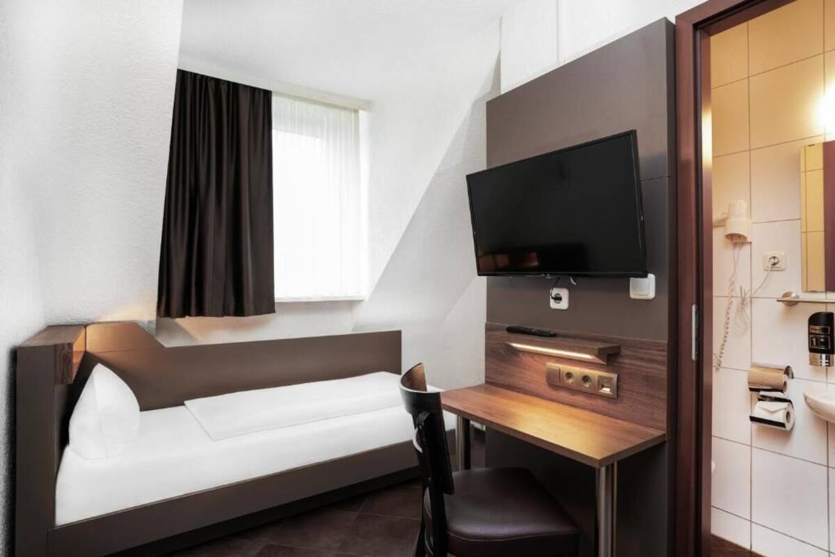 Ein modernes Hotelzimmer mit Schlafsofa, Schreibtisch mit Flachbildfernseher, kleinem Tisch und Spiegel.