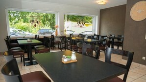 Un restaurant doté de nombreuses tables et chaises, de grandes fenêtres offrant une vue sur les voitures garées et la verdure environnante.
