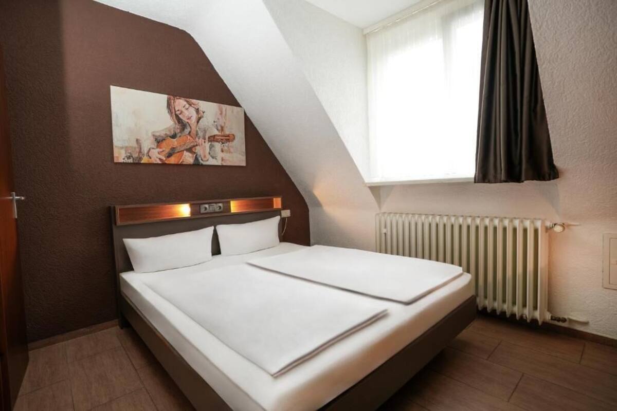 Ein Schlafzimmer mit Bett, Kopfstütze, einem Gemälde, einem Fenster mit Vorhängen und einem Heizkörper.