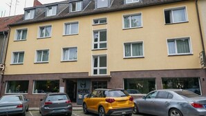 Een meerlaags hotel met een gele gevel, meerdere ramen en een parkeerplaats met auto's.