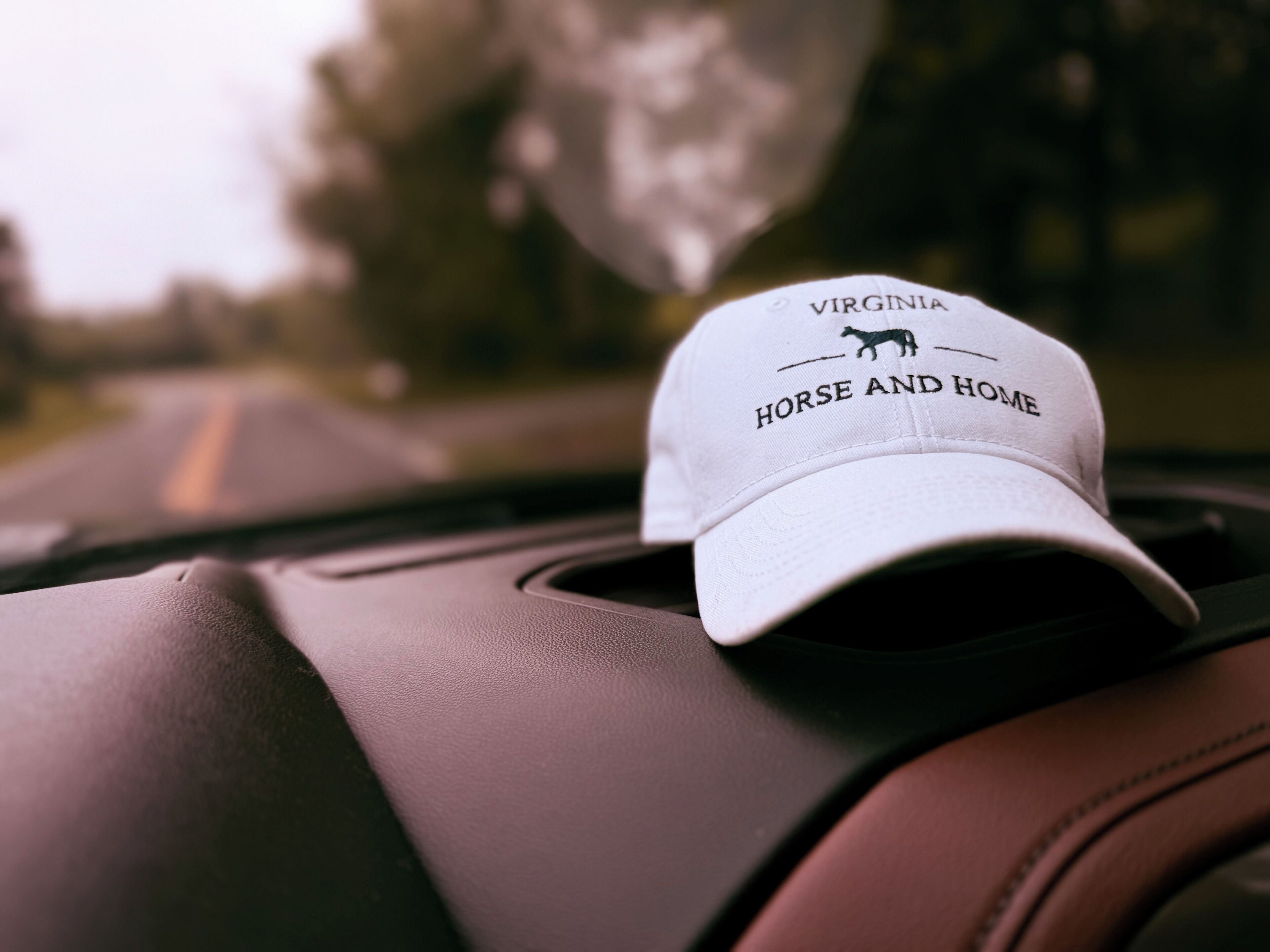 A white cap with 'Virginia Horse and Home' text and a horse silhouette on a car dashboard.