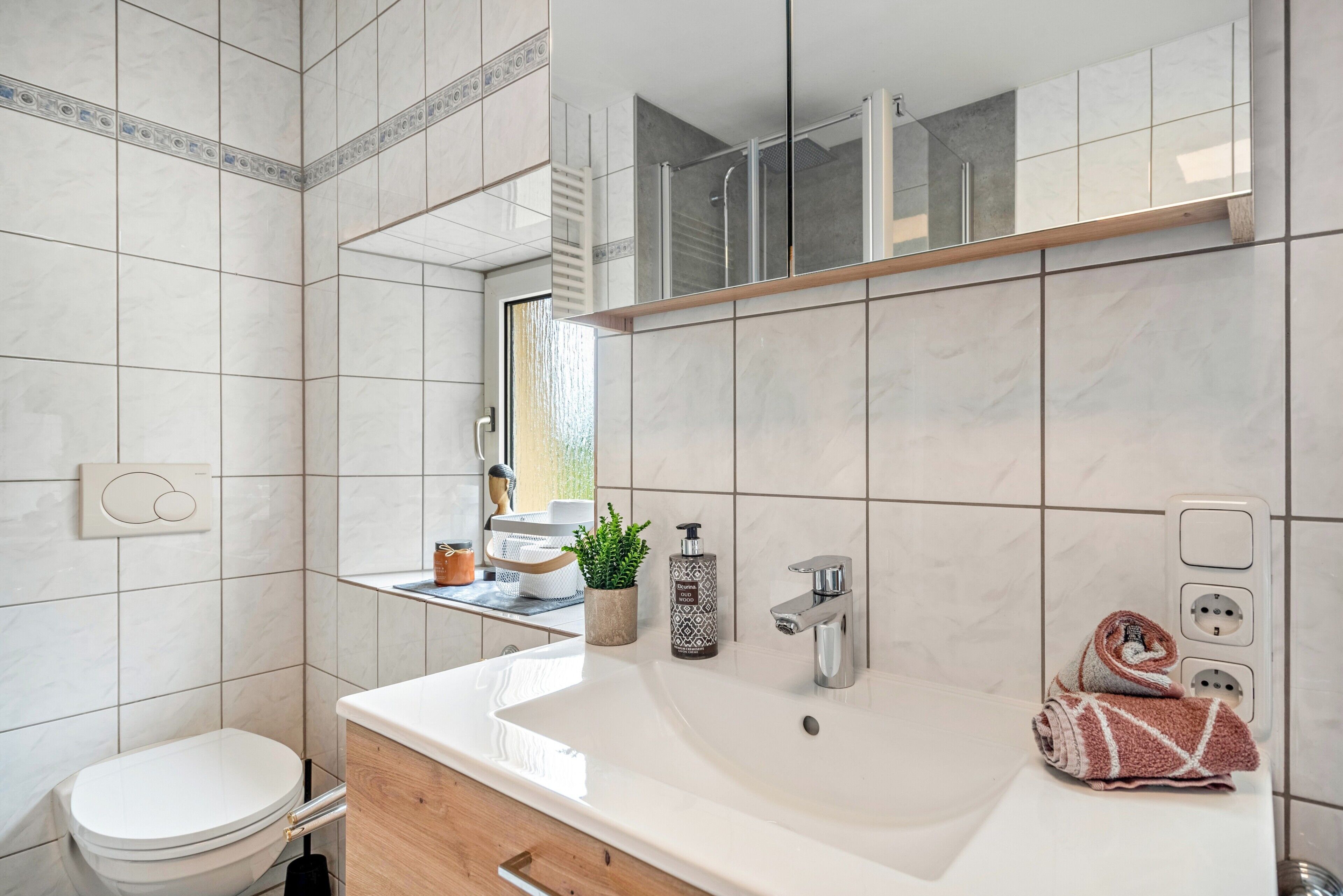 A bathroom with a white sink, a toilet, a mirror, and a towel on the counter.