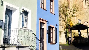 Une rue bordée d’un immeuble doté d’une tour horlogère, d’une façade bleue et d’un bâtiment vert avec une porte blanche.