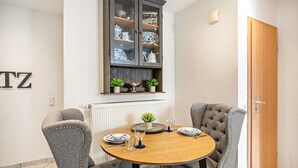 Un coin repas comprenant une table ronde, deux chaises grises à revêtement rembourré, un buffet contenant de la vaisselle et une porte en bois.