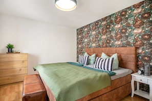 Une chambre à coucher comprenant un lit, une commode, une table de chevet et un mur orné d’un motif floral.