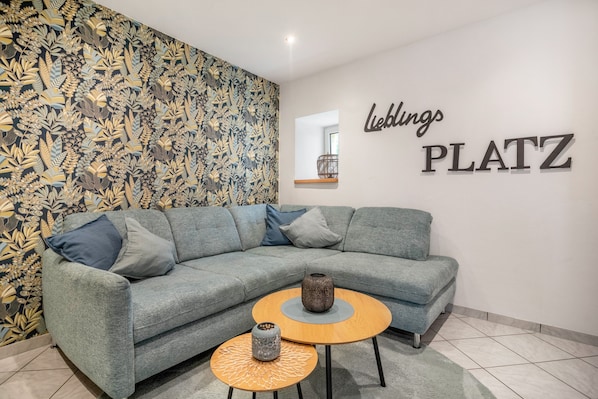Un salon avec un canapé gris, deux petites tables rondes et un mur orné d’une enseigne « Ledlings PLATZ ».