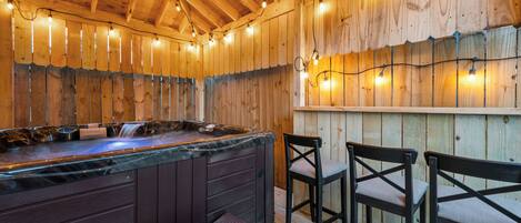 A wooden interior with a hot tub, wooden chairs, and string lights.