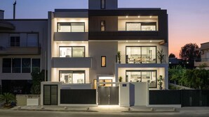 Um edifício residencial moderno de dois andares, com amplas janelas, varanda e portão fechado.