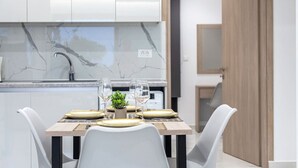 Uma cozinha moderna com armários brancos, painel de fundo de mármore e área de jantar com mesa de madeira e cadeiras brancas.