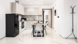 Uma cozinha moderna com geladeira preta, armários brancos e bancada de mármore.