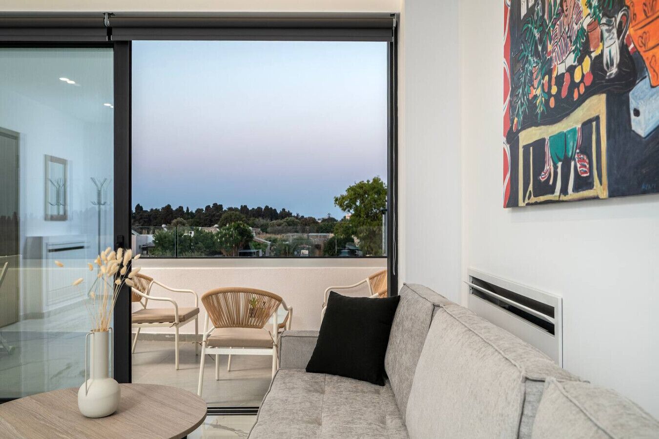 A modern living room with a large sliding glass door leading to a balcony with a city view.