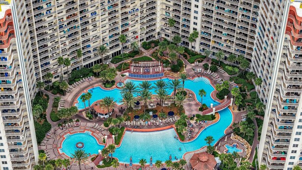 An aerial view of a hotel with multiple swimming pools, palm trees, and a central pavilion. - Shores 1613-King Bed-Beachfront Resort & Amenities (Panama City Beach)