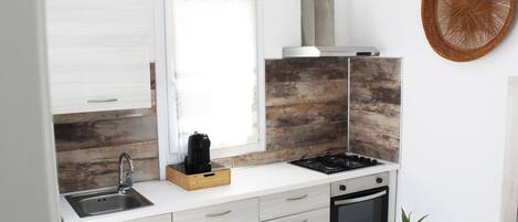 A modern kitchen with a built-in stove, sink, and oven, featuring light wood cabinetry and a large window.