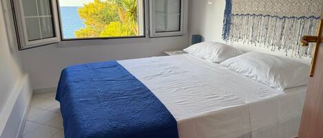 A bedroom with a bed, a view of the sea through a window, and a decorative headboard.