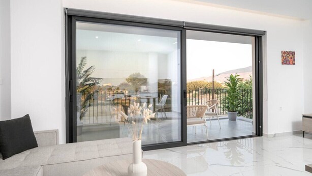 A modern living room with a large sliding glass door leading to an outdoor patio. - Icon Luxury Apartments : A2 (Kos)