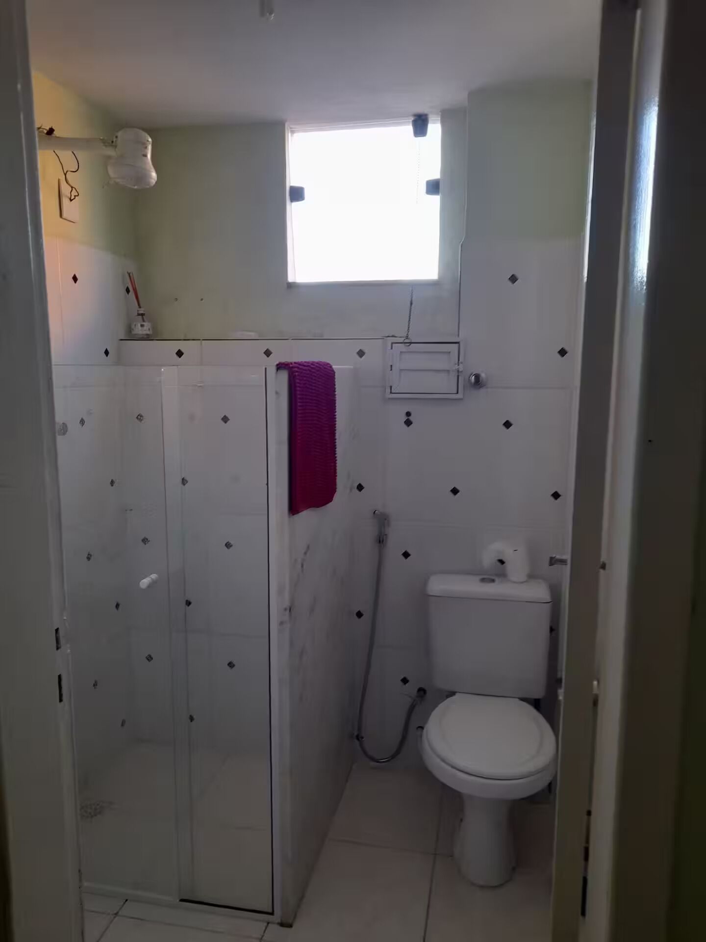 Un baño con cabina de ducha de vidrio, un inodoro y una ventana pequeña.