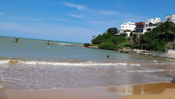 A beach with clear water, a few boats, and buildings on a hill. - Suite 303 beach walking distance (Anchieta)