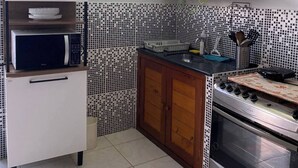 A kitchen with white cabinets, a microwave, a stove, and a tiled backsplash. - Suite 303 beach walking distance (Anchieta)