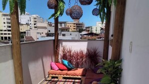 A small balcony with a wooden pergola, hanging decorative balls, a cushioned seating area with colorful cushions, a small table with a plant, and a striped rug. - Suite 303 beach walking distance (Anchieta)