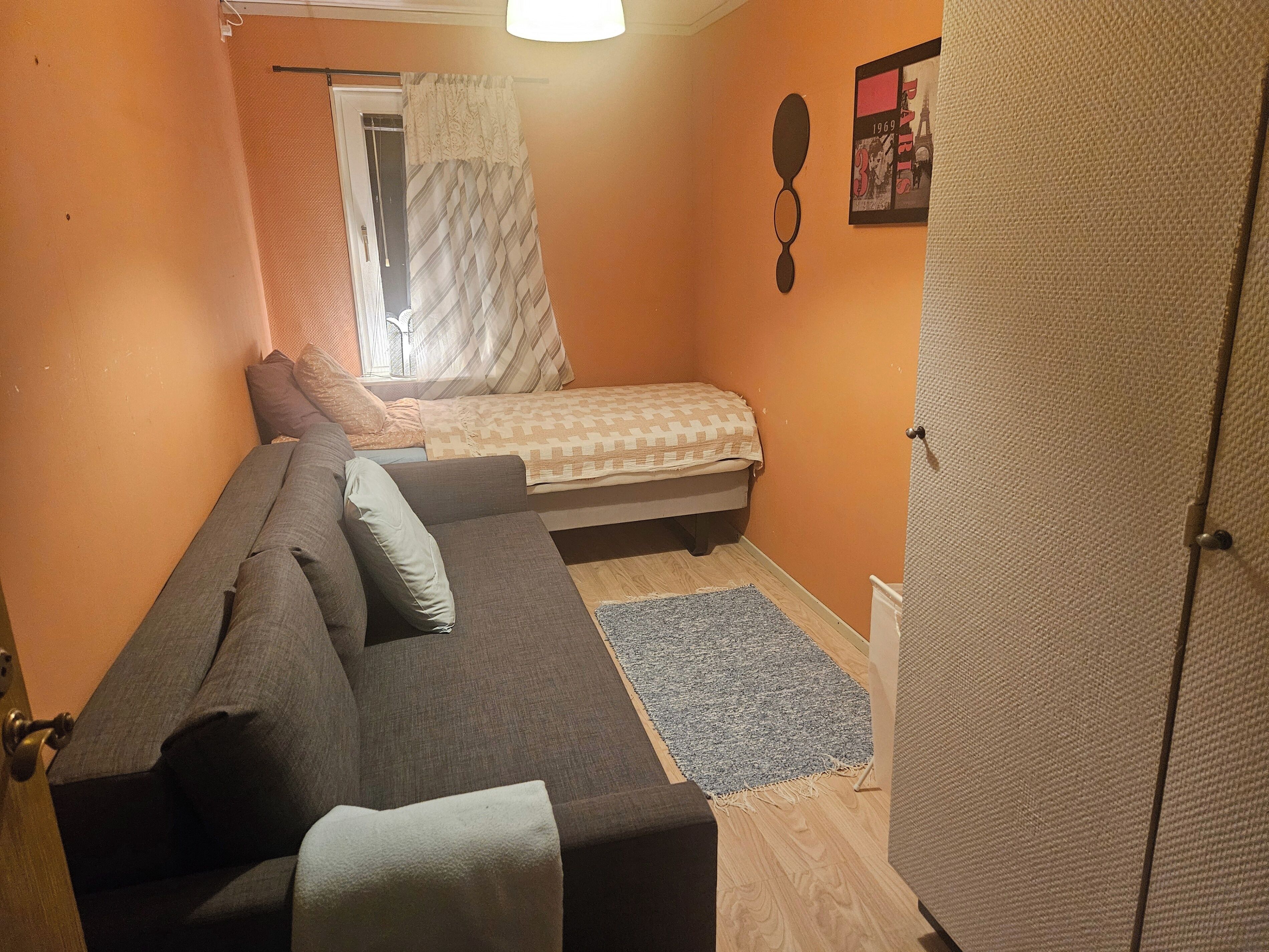 A small, compact room with a bed, a sofa, and a wardrobe.