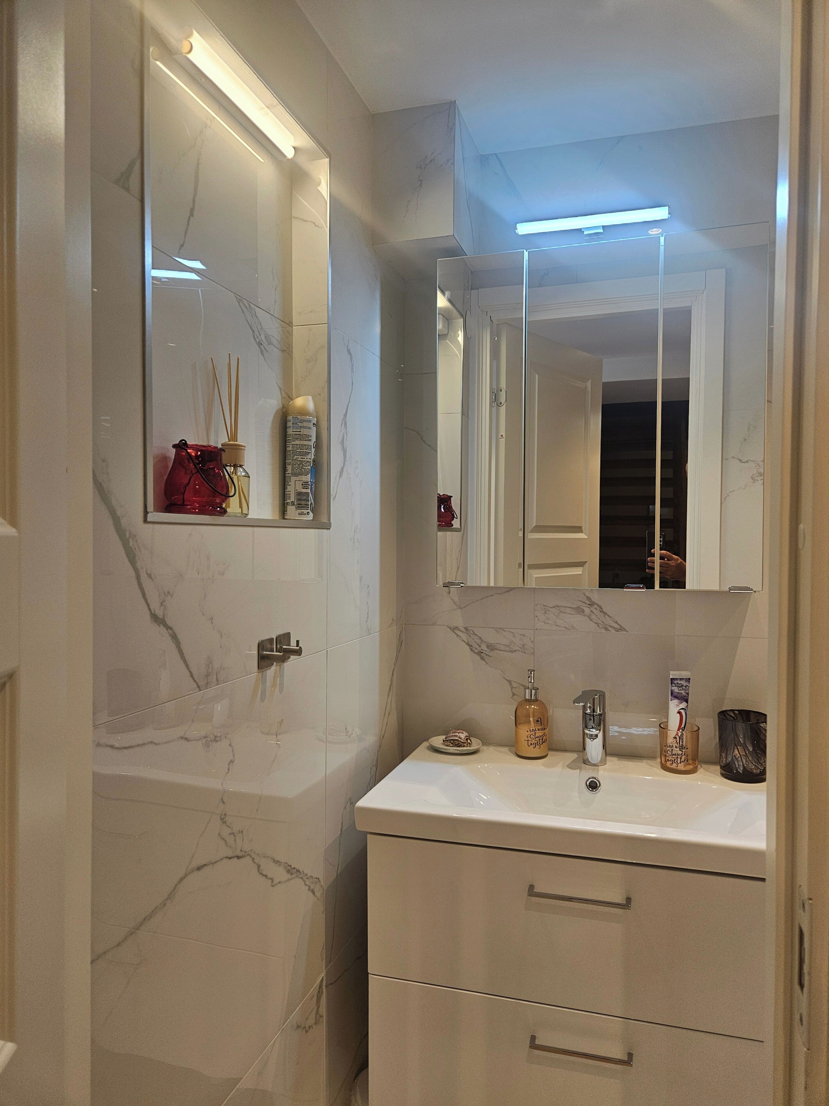 A bathroom with a marble sink, a mirror, a vanity with drawers, and a towel rack.