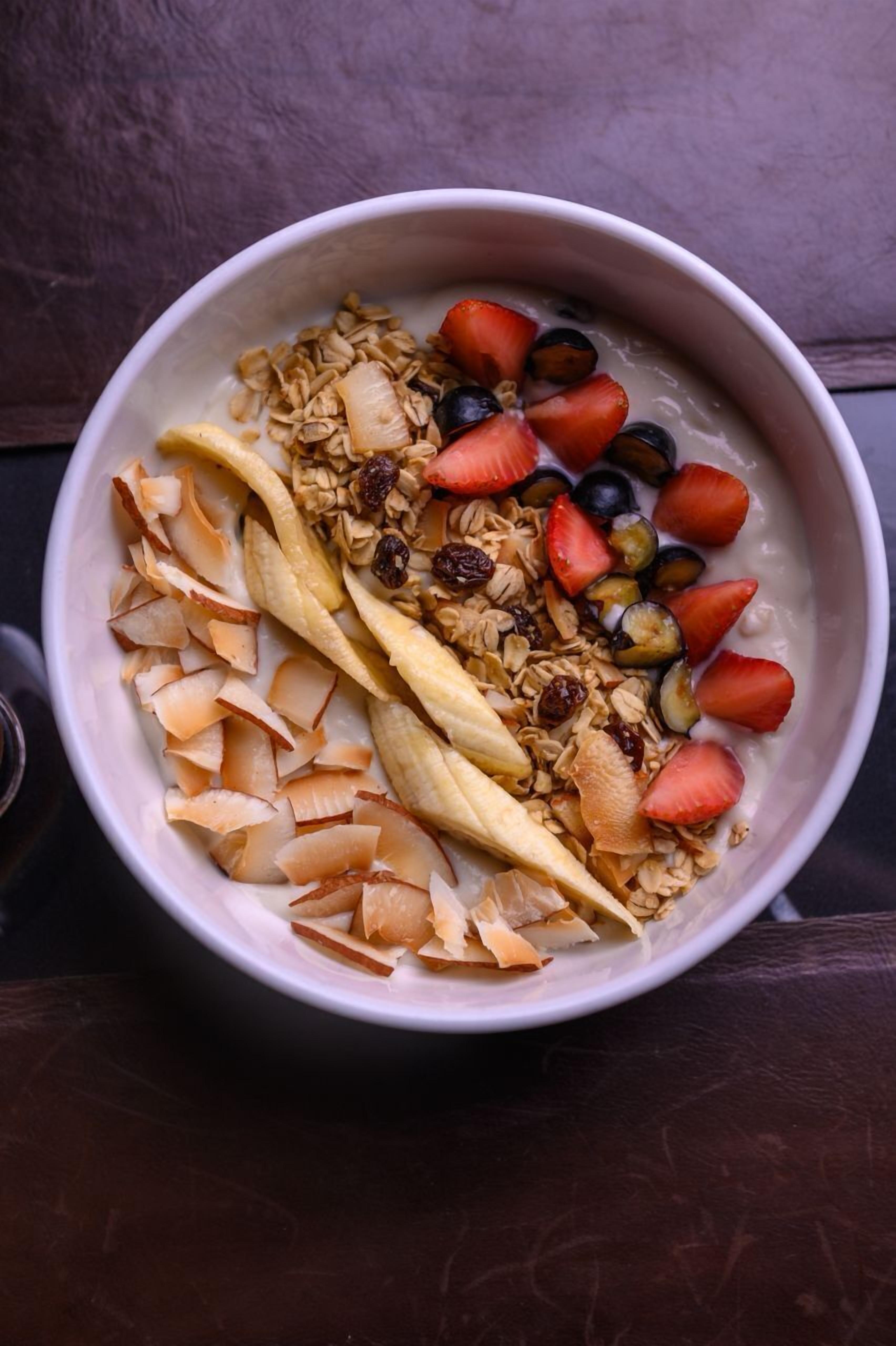 A bowl of oatmeal with sliced bananas, strawberries, blueberries, and coconut flakes.