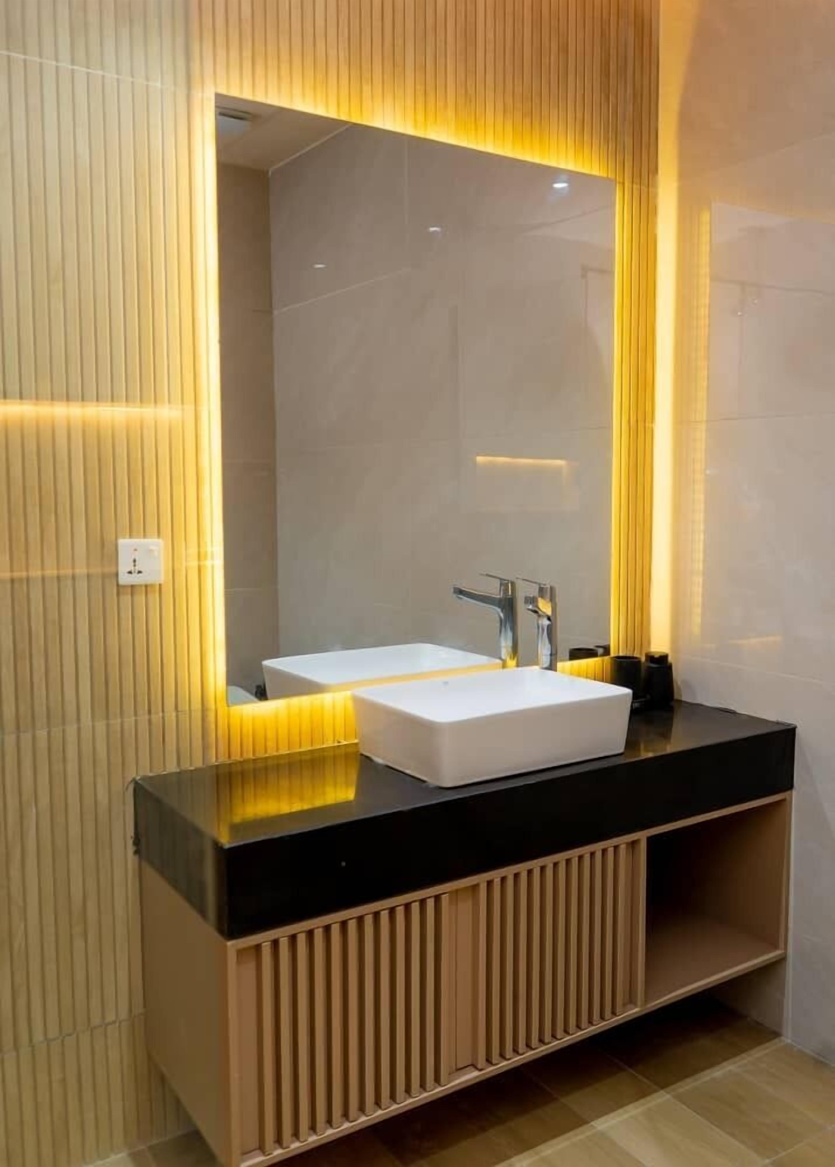 Un baño moderno con un lavamanos rectangular, un espejo grande y una encimera negra.