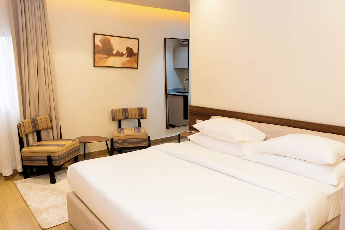 A hotel room with a large bed, a chair, a small table, a mirror, and a painting on the wall.