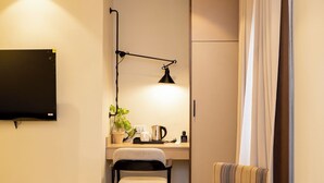 A compact hotel room with a bed, a desk with a chair, a TV, and a small table. - 7EVEN Suites (Lekki)
