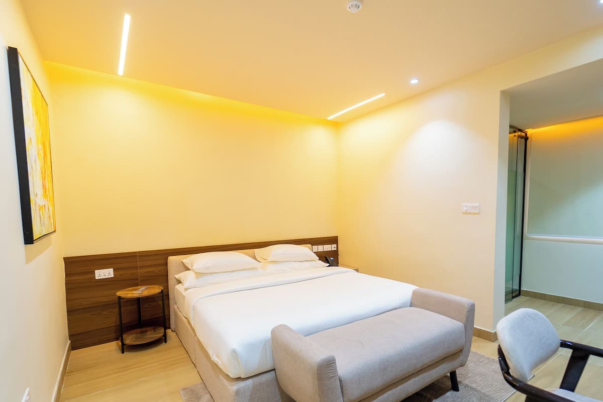 A modern hotel room with a large bed, bedside tables, a chair, and a view of the hallway.