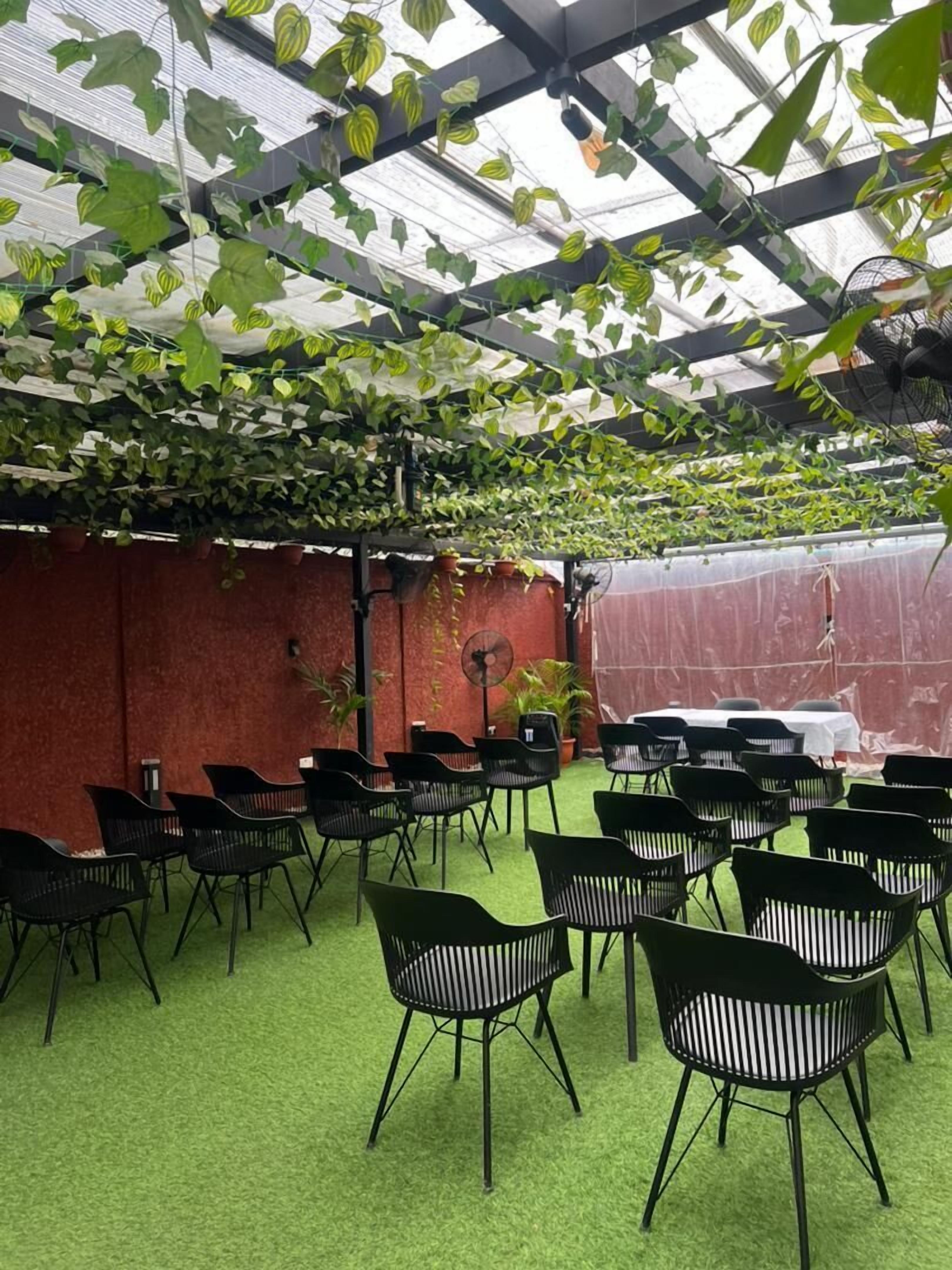An indoor garden area with a green artificial turf floor, black metal chairs arranged in rows, and hanging plants.