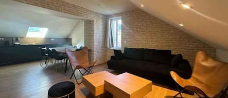 A loft-style living area with a black leather sofa, wooden coffee table, and a dining table with chairs.
