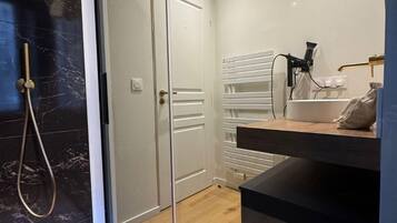 A modern bathroom with a marble shower wall, a white door, and a wooden vanity with a towel rack.
