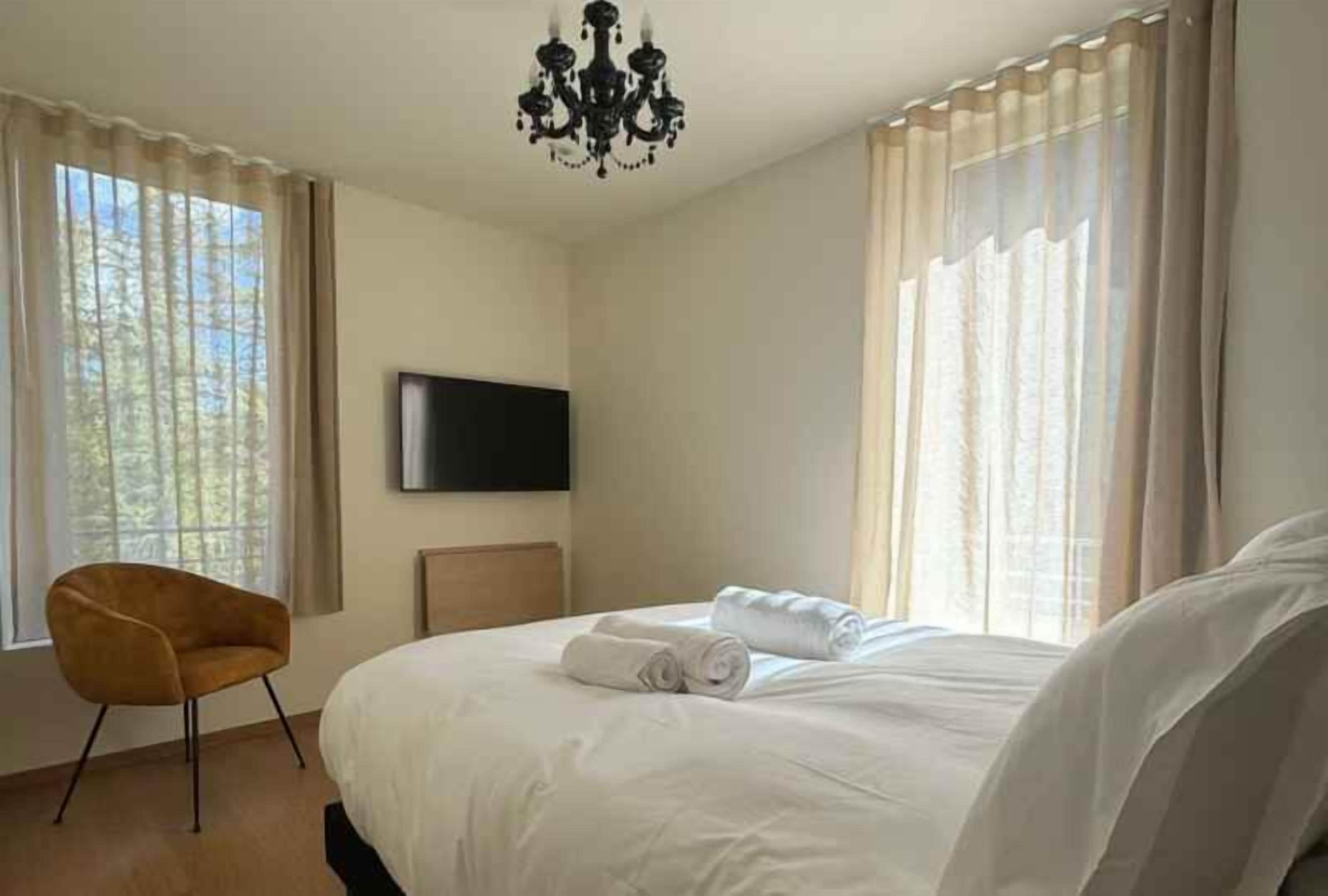 A hotel room with a bed, a chair, a television, and curtains.